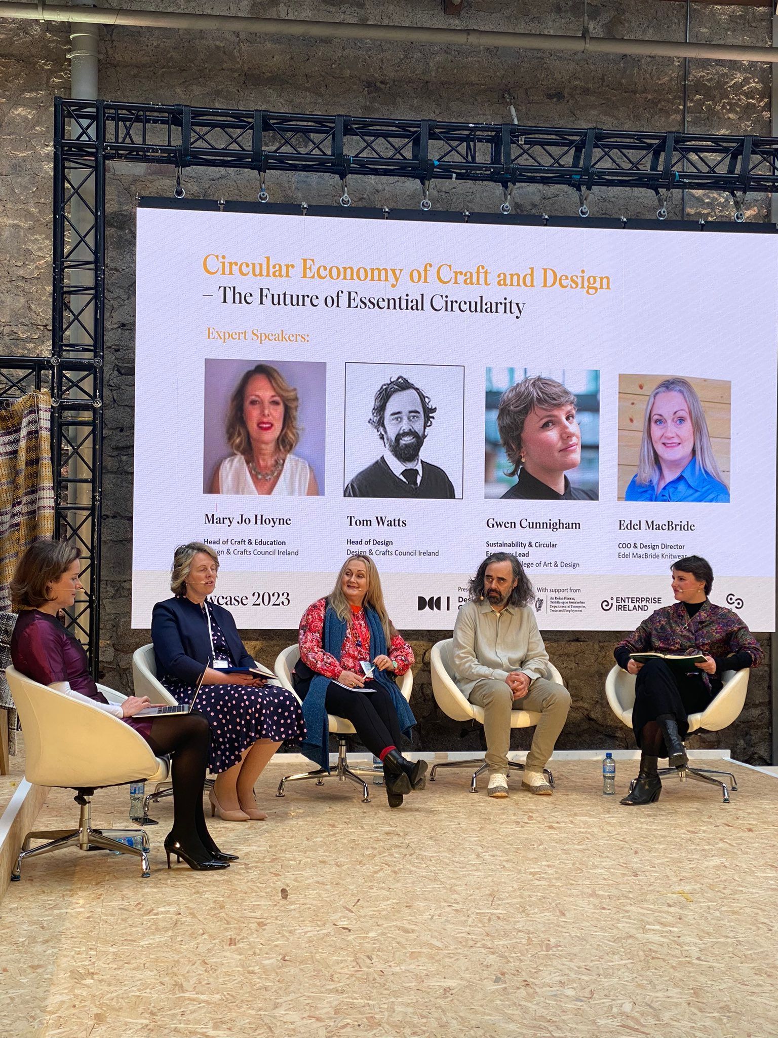 Panel discussion on stage before a banner with speaker portraits at a conference venue