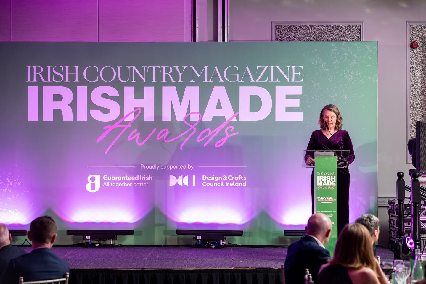 Irish Country Magazine awards stage with presenter at podium and purple-lit backdrop reading “Irish Made Awards”