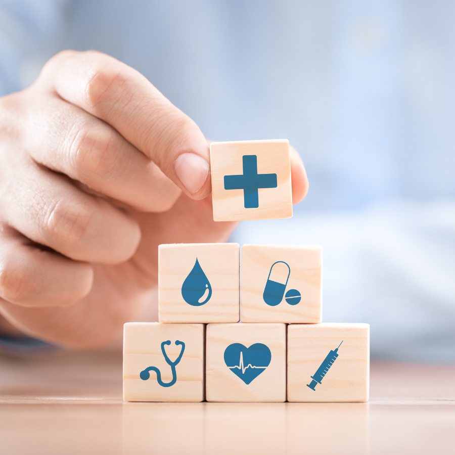 Hand holding medical cross cube over stacked wooden blocks with health icons on a light background