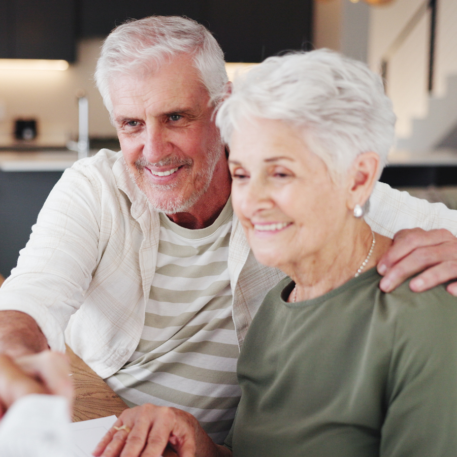 Smiling couple seated together indoors, leaning close while looking at something off-camera