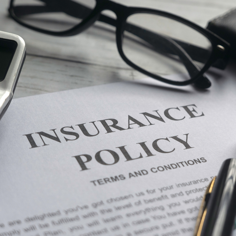 Insurance policy document on a desk with eyeglasses and a pen nearby
