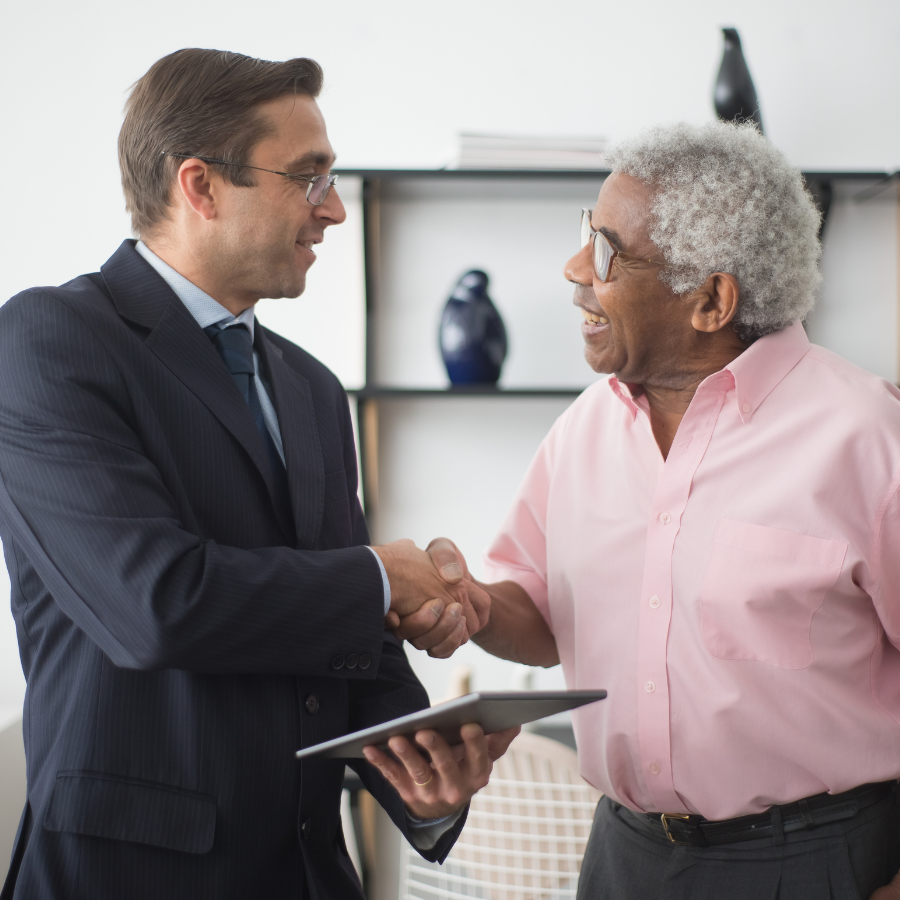 Two professionals shaking hands in an office, one holding a tablet.