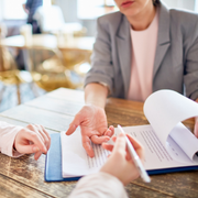 Colleagues reviewing paperwork at a wooden table, with one person gesturing and another holding a pen.