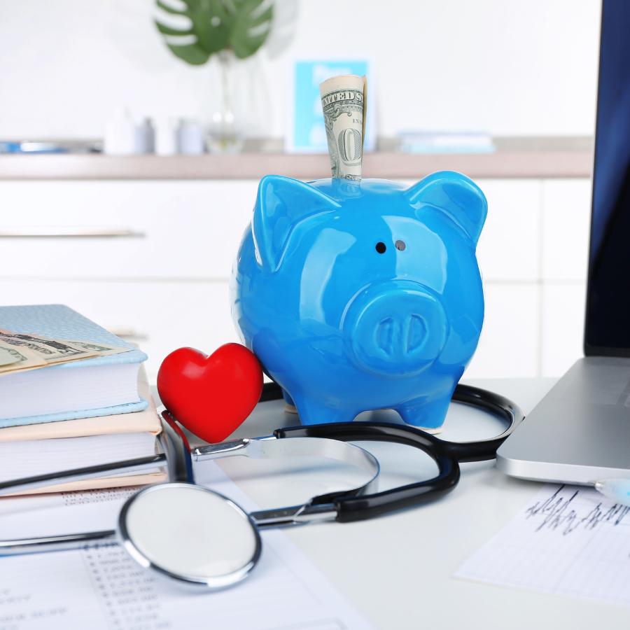 Blue piggy bank with cash, stethoscope, and red heart on a desk, suggesting healthcare savings