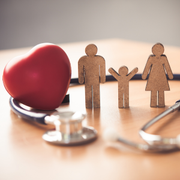 Red heart beside wooden family figures with stethoscope on a table