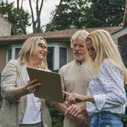 Three people reviewing a document outdoors in front of a house