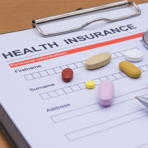 Health insurance form on a clipboard with assorted pills scattered across it