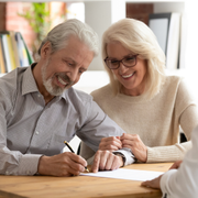 Smiling couple reviewing documents together at a table, one writing with a pen