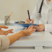 Patient speaking with a doctor at a desk during a consultation, hands gesturing over paperwork