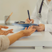 Patient speaking with a doctor at a desk during a consultation, hands gesturing over paperwork