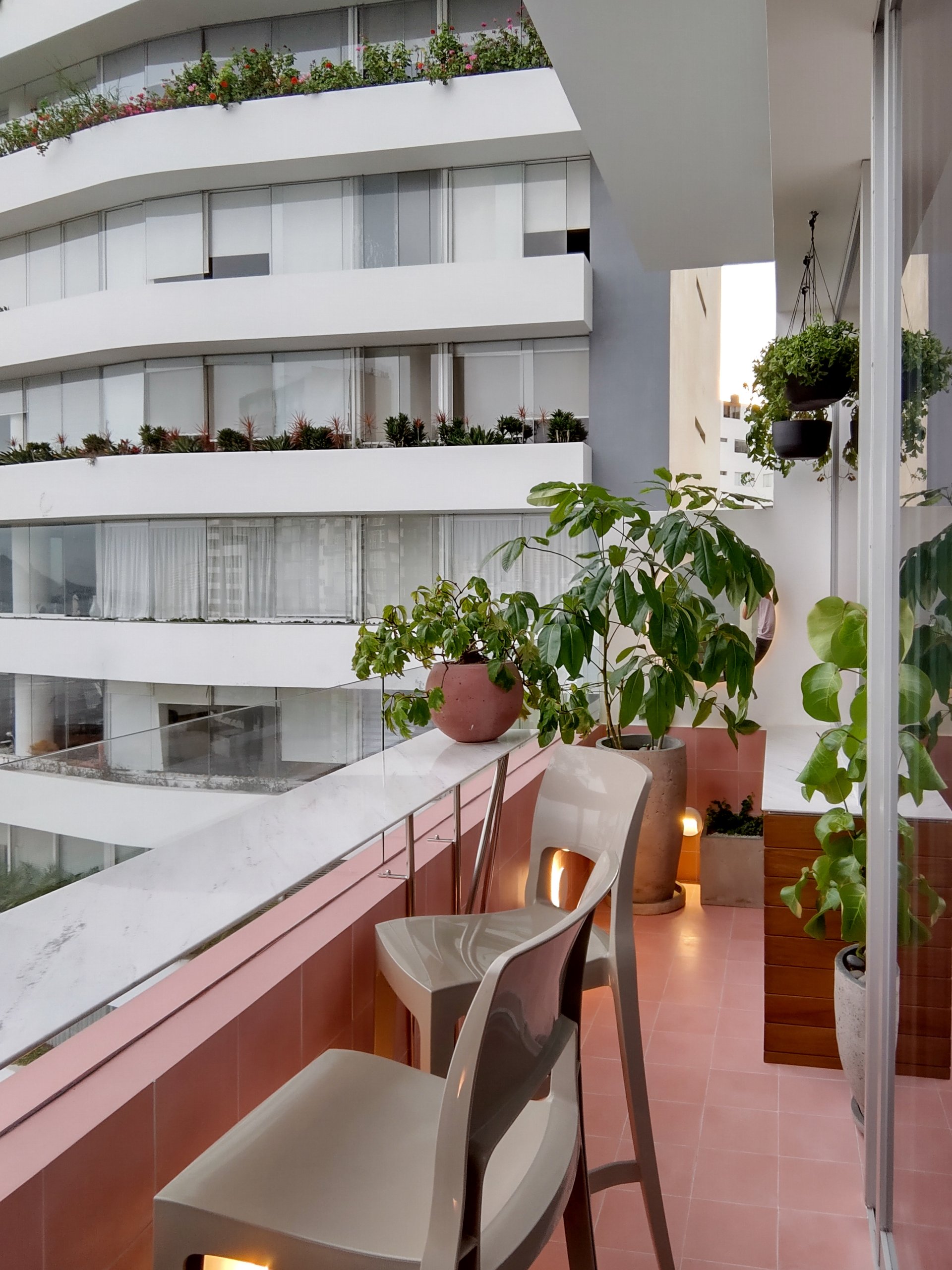 Un balcón con sillas y plantas en macetas frente a un edificio.