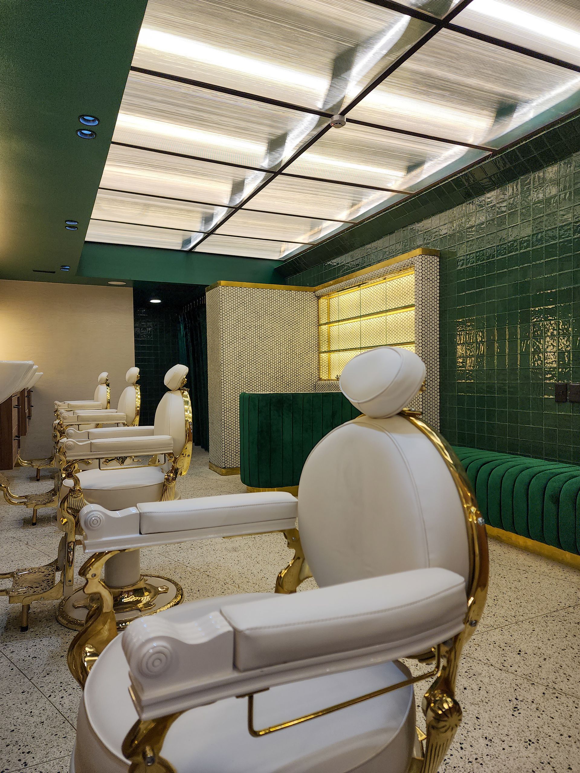 Una fila de sillas blancas y doradas en una habitación con una pared verde.