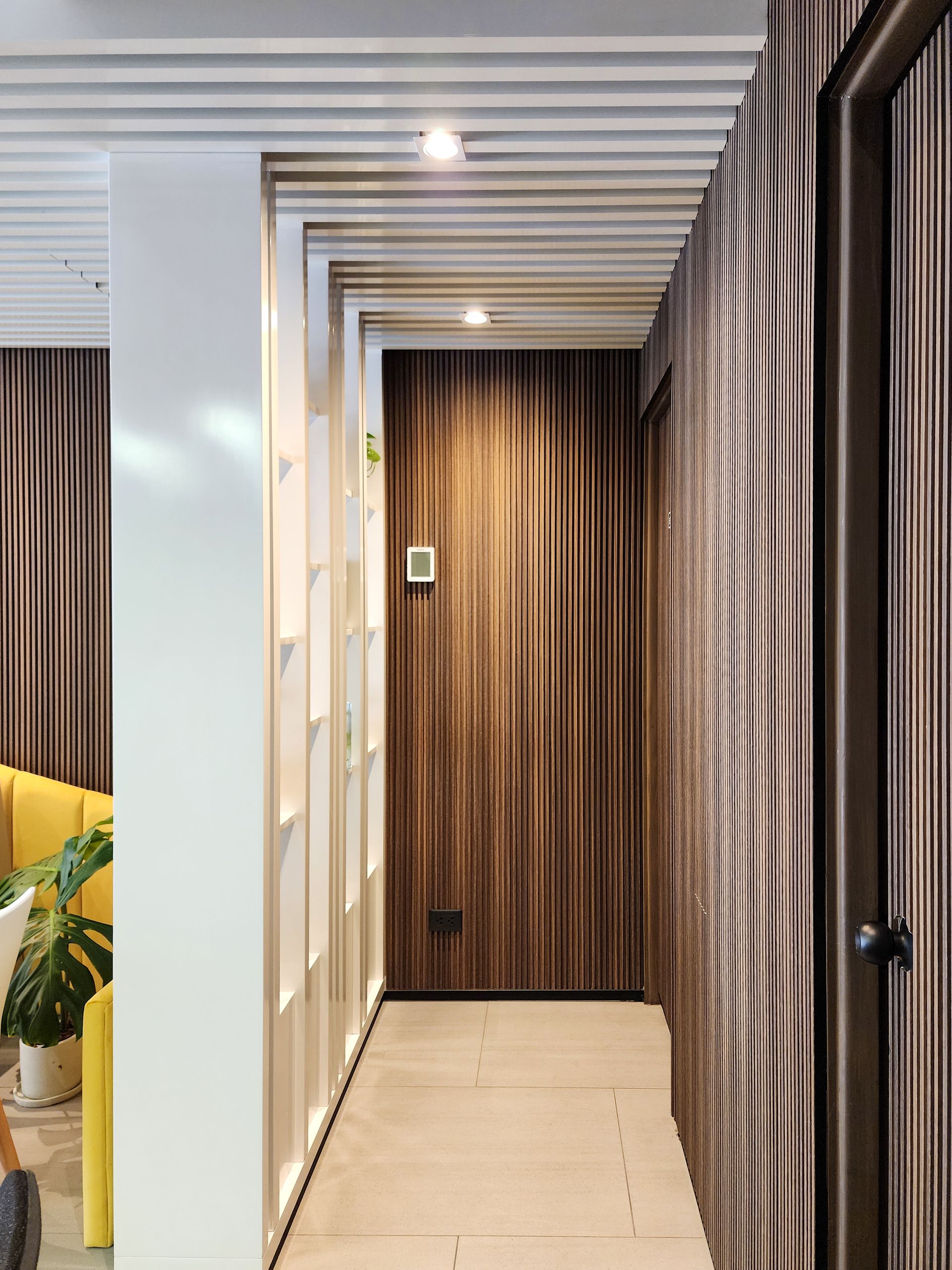 Un largo pasillo con una puerta de madera y una silla amarilla.