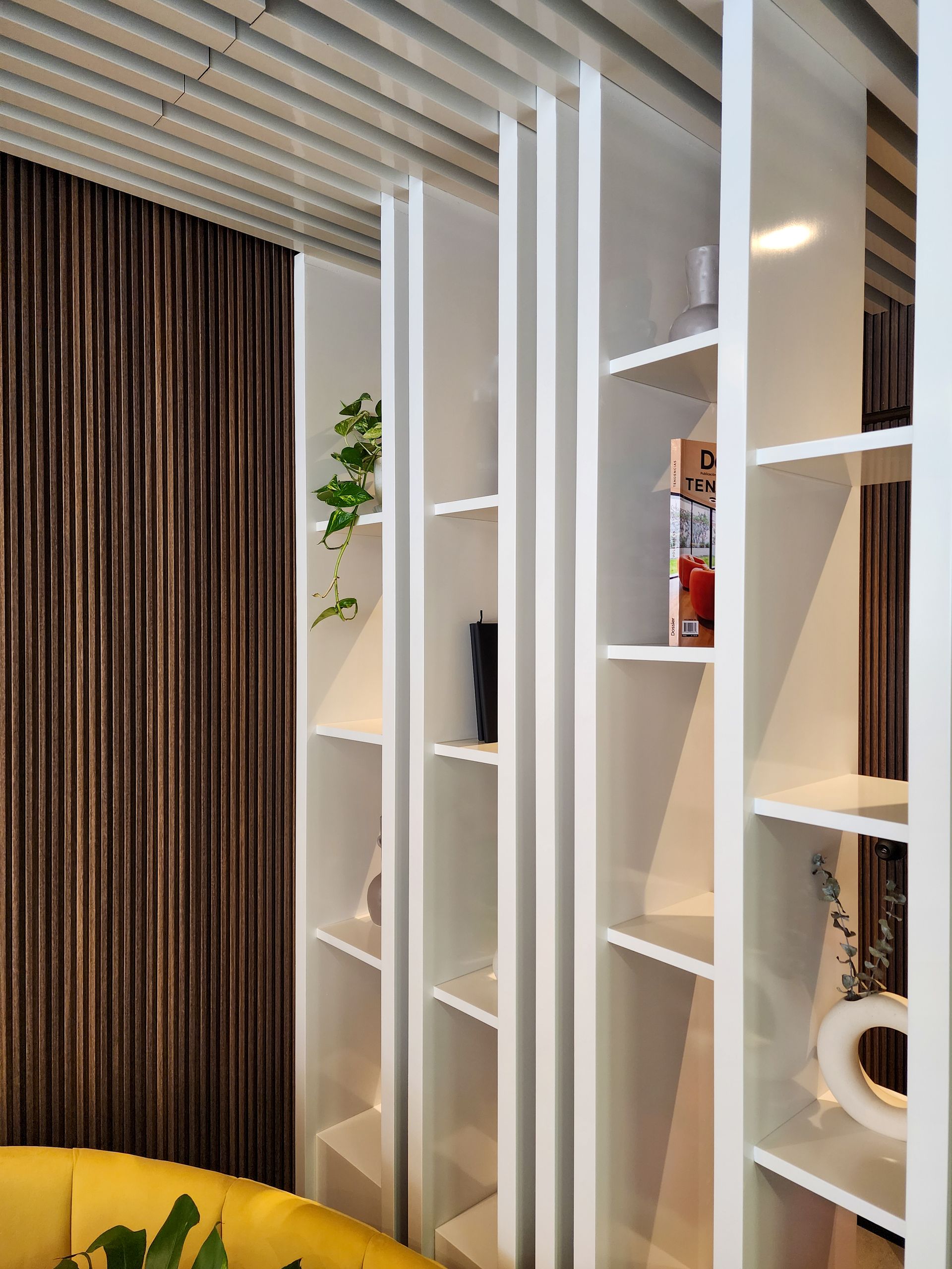 Una sala de estar con estantes blancos y un sofá amarillo.