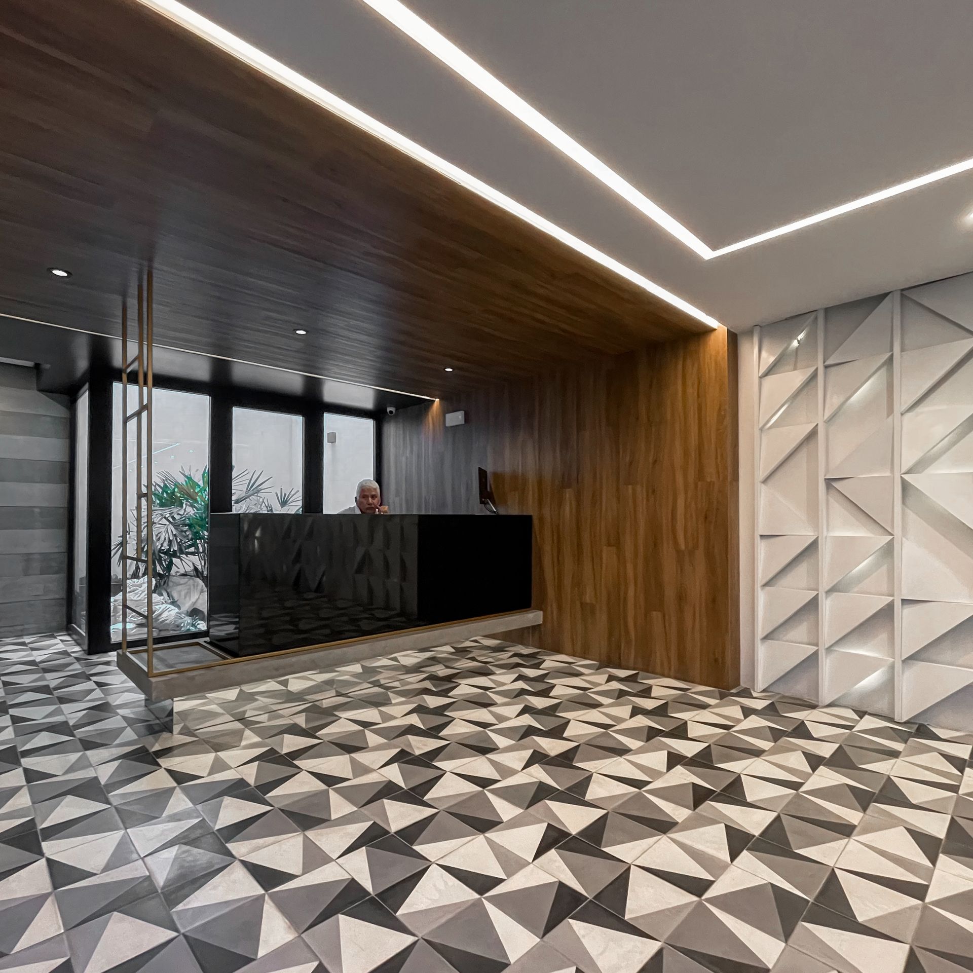 Un hombre está sentado en un escritorio en un vestíbulo con un suelo con dibujos geométricos.