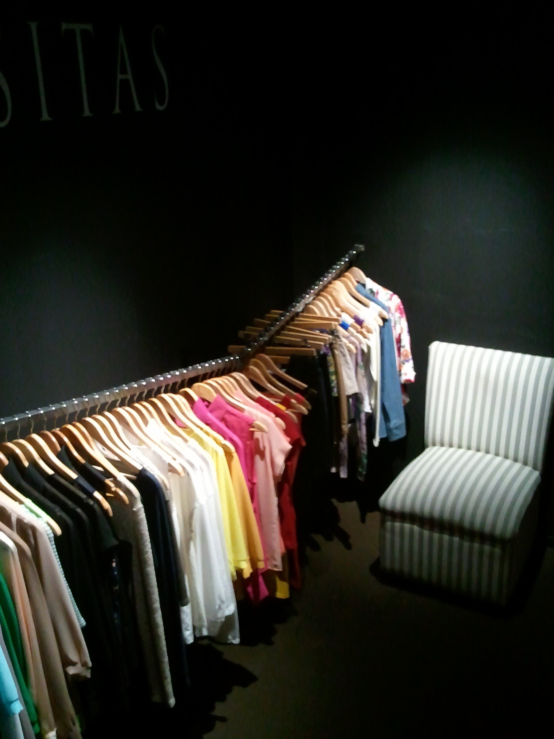Una silla se encuentra frente a un perchero con ropa debajo de un cartel que dice 