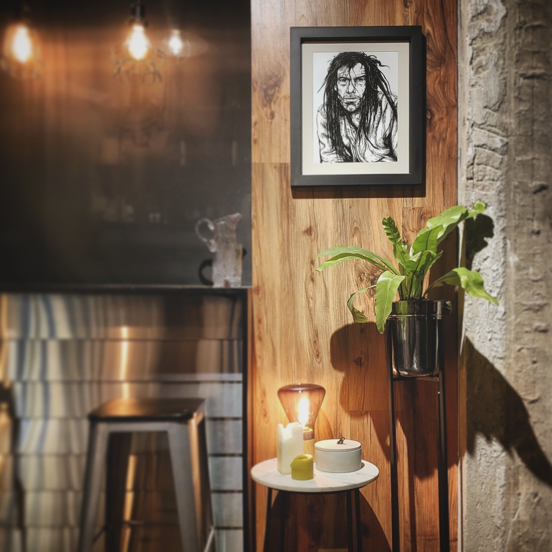 Una imagen de un hombre está colgada en una pared de madera sobre una mesa con velas y una lámpara.