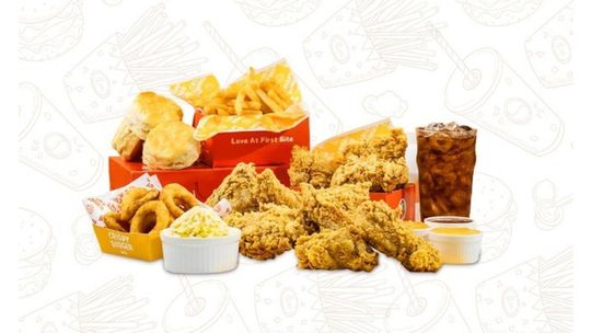 Assorted fried chicken pieces with sides and dipping sauce, arranged on a white background.