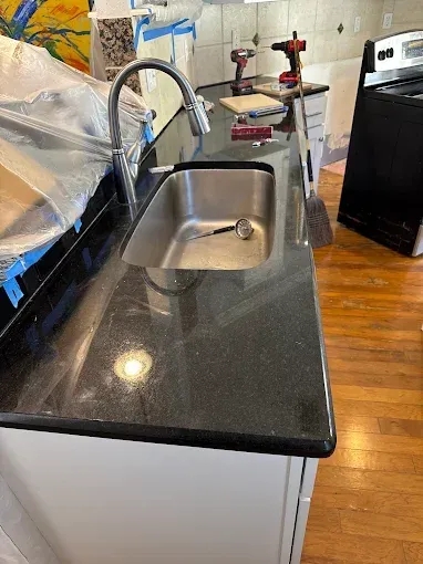 Kitchen with black granite countertop, stainless steel sink, and tools, undergoing renovation.