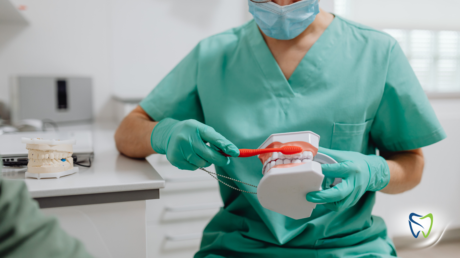 Dentist in green scrubs demonstrating teeth brushing technique with a model.