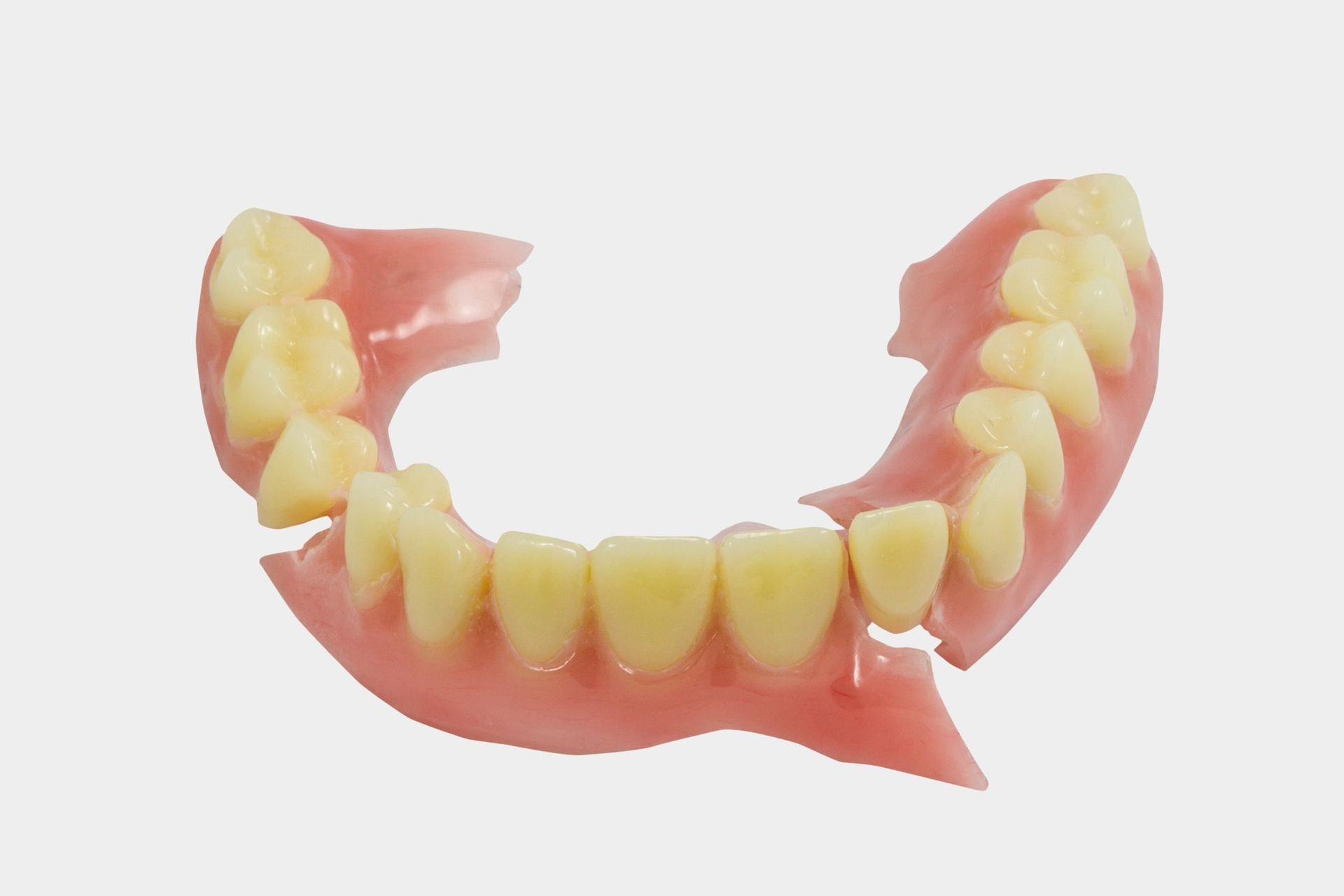 A close up of a broken denture with teeth on a white background.