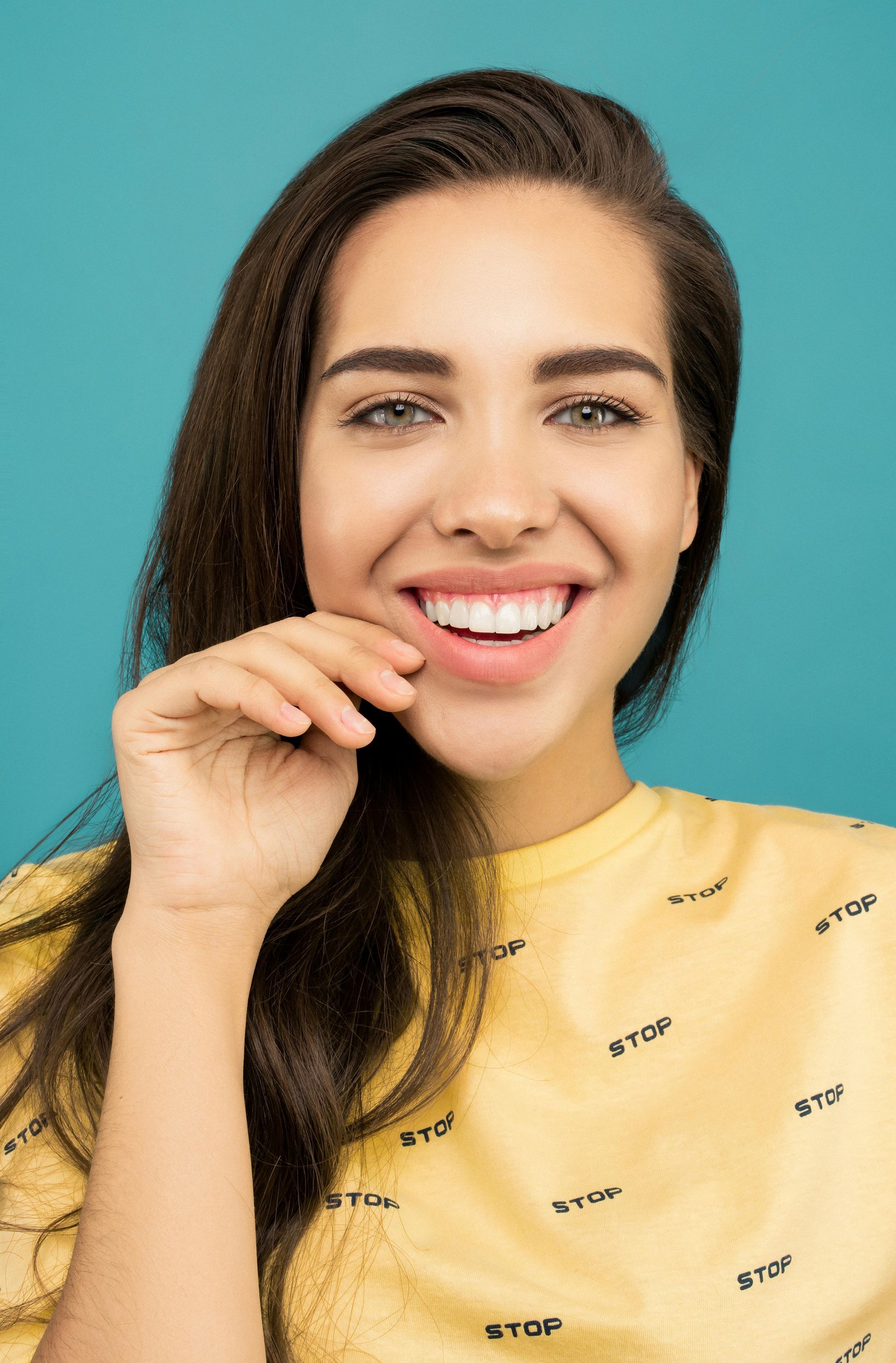 A woman in a yellow shirt is smiling and touching her face.
