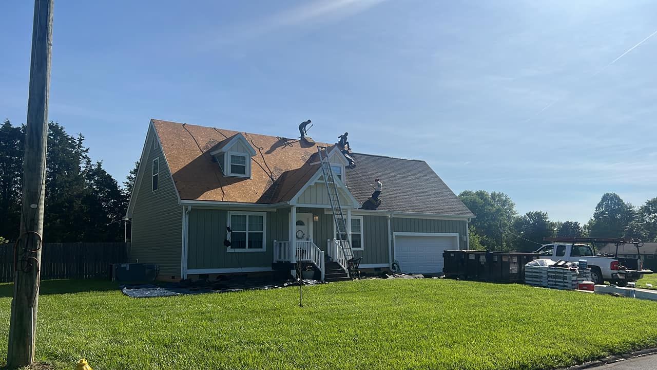 Workers on a roof replacing shingles of a green house on a sunny day.