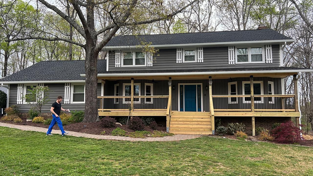 Two-story house with gray siding, blue door, and large front porch. Person walks on a path.