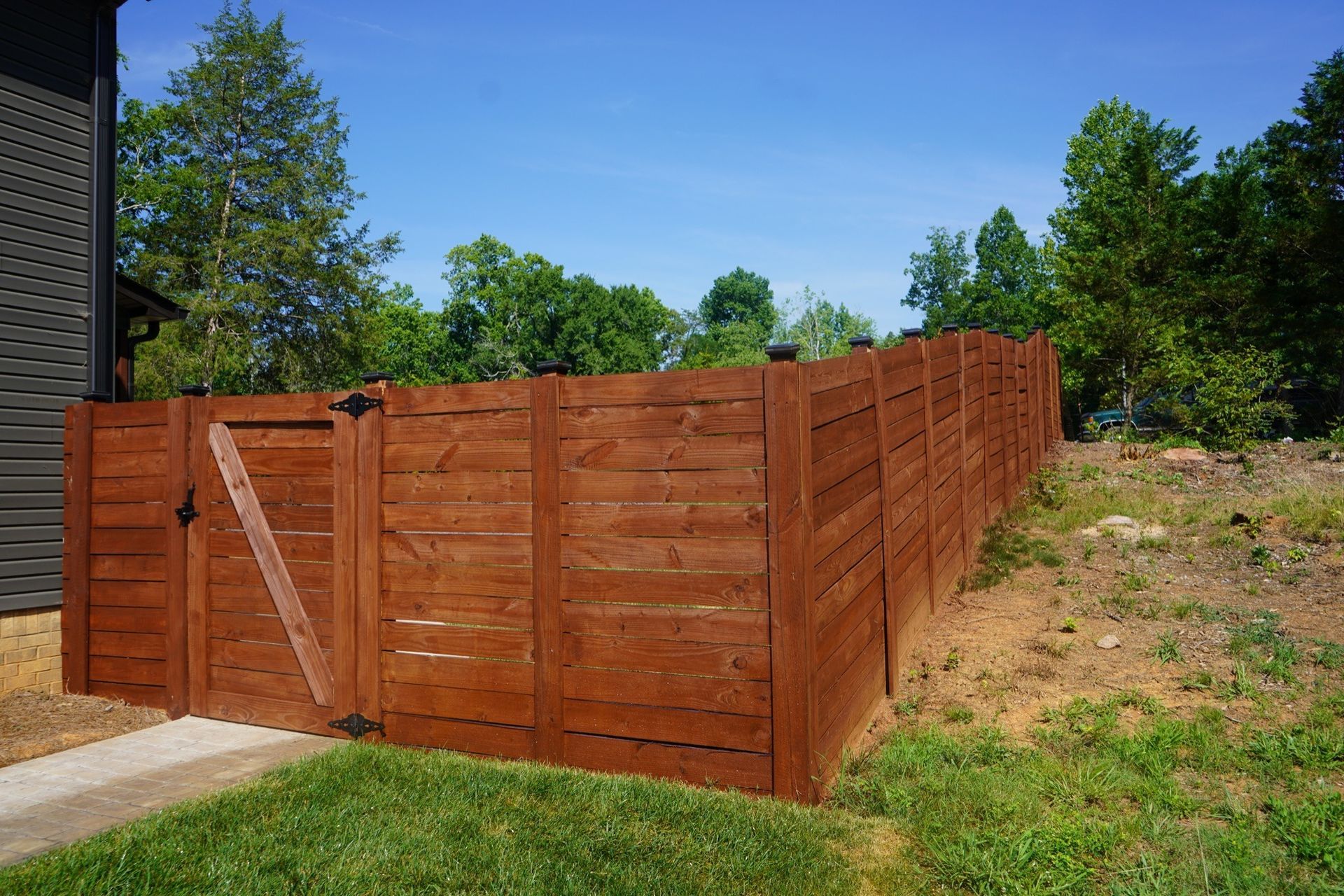 Brown wooden fence with a gate, next to a building and grass, under a blue sky.