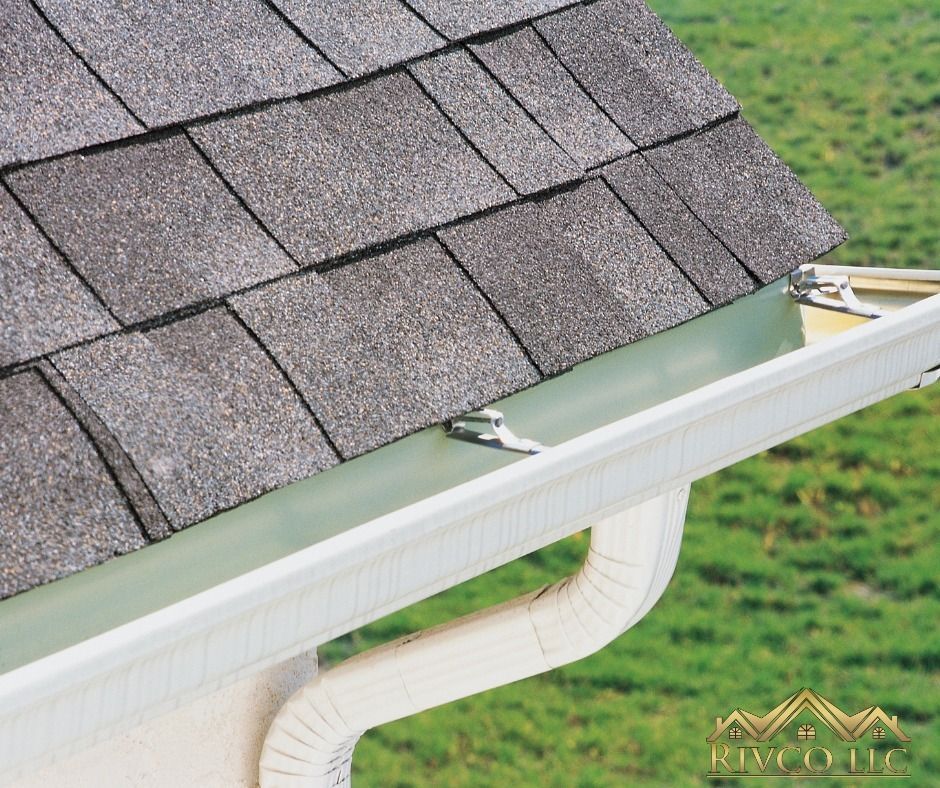 Close-up of a house roof and white gutter. Shingle roof over a green gutter area, gutter angles down.