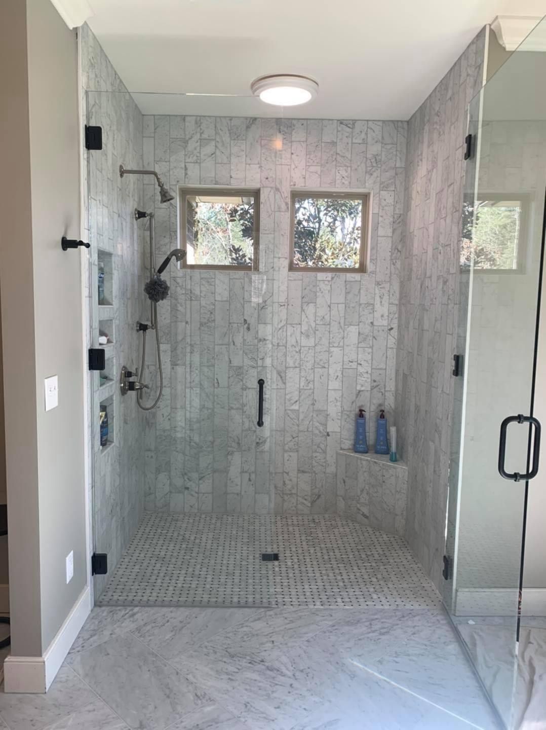 Modern shower with glass doors, gray tile, and multiple showerheads.
