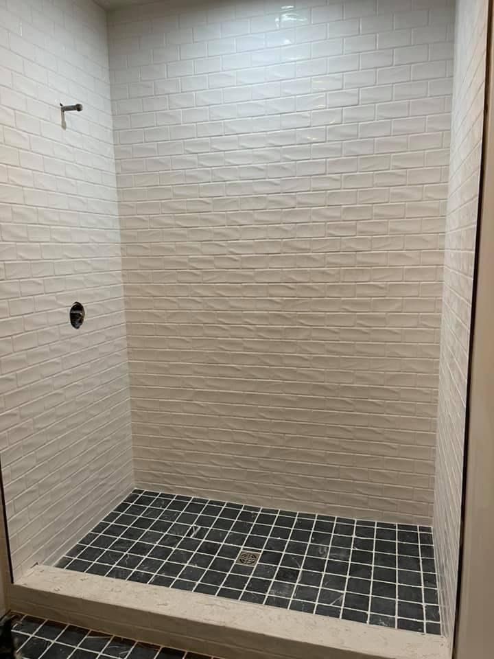 White tiled shower with textured wall, black and white floor tiles.