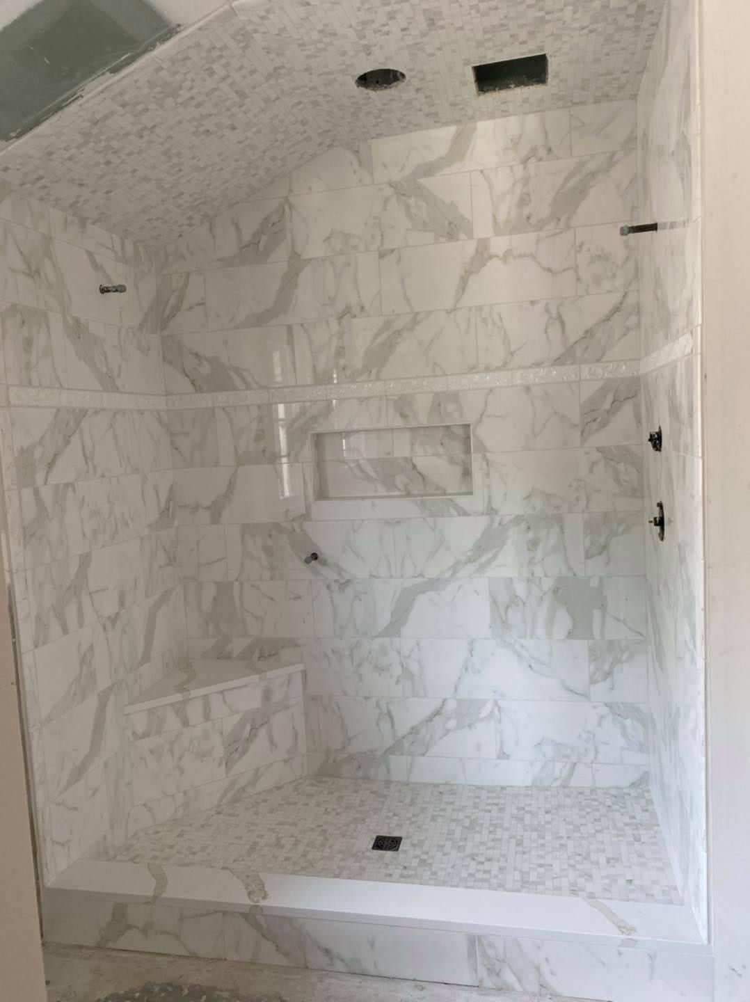 Marble-tiled shower with a built-in bench and recessed shelf. Glass doors and pebble floor.