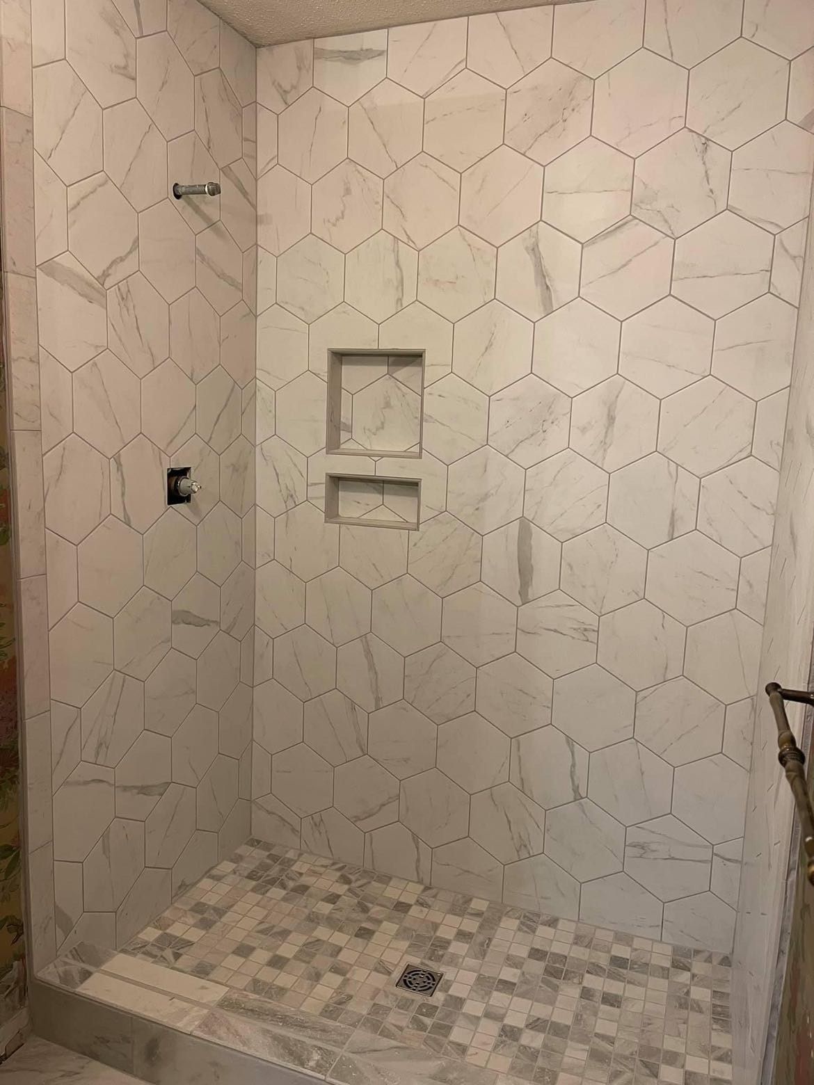 White hexagon tile shower with two built-in niches. Gray mosaic tile shower floor. Shower fixtures installed.
