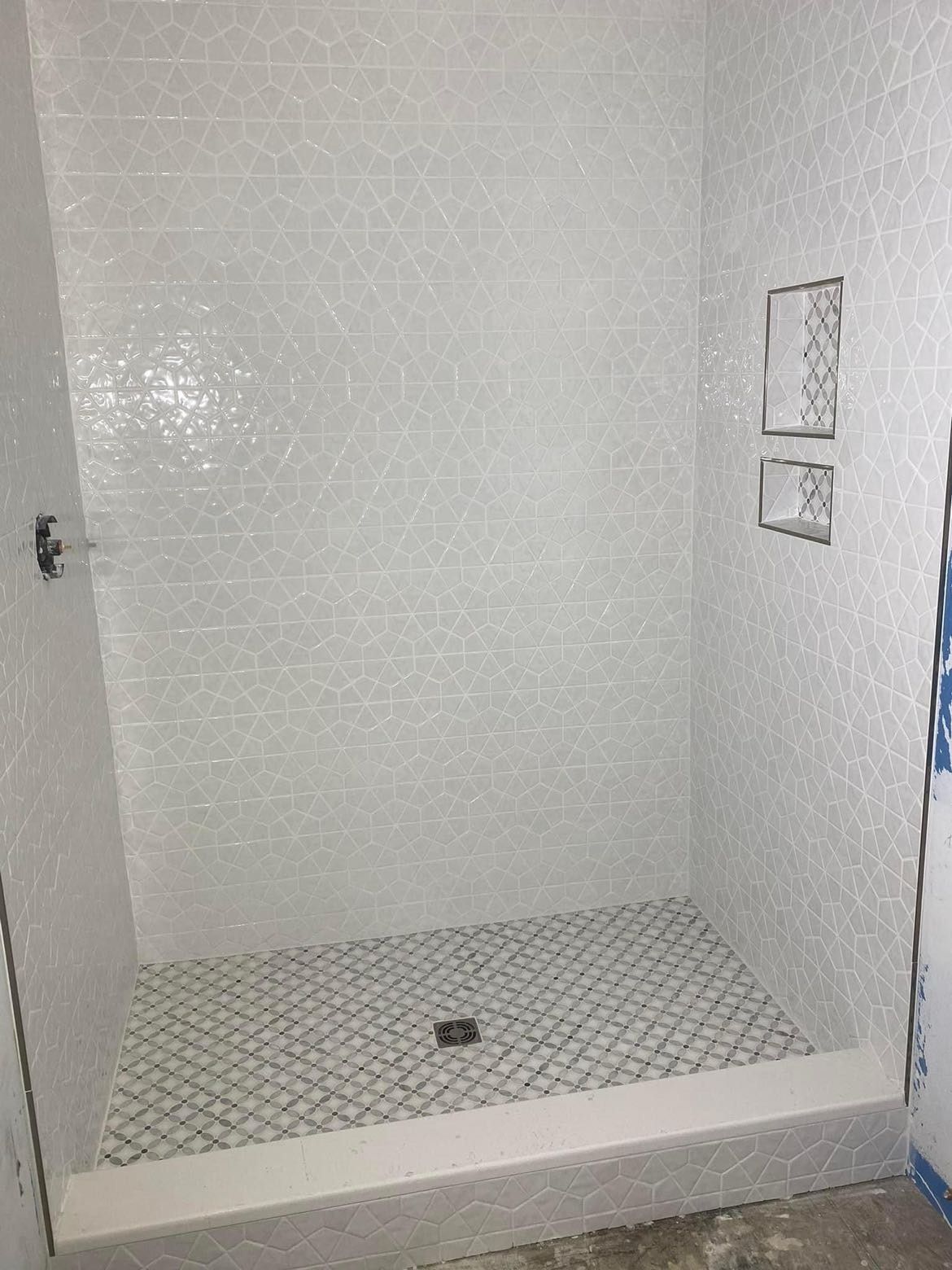 White tiled shower with built-in shelves; black and white patterned floor.