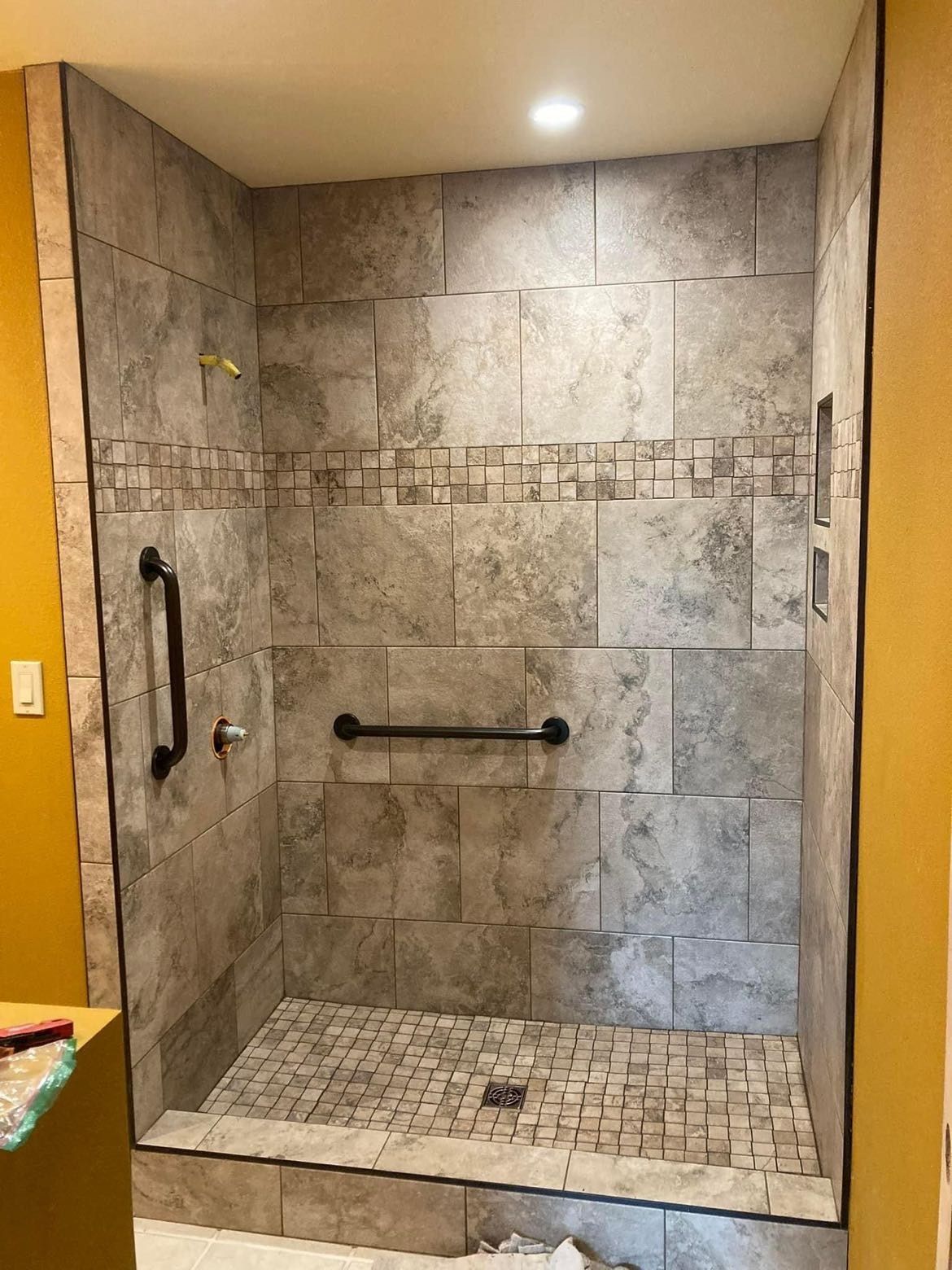 Finished shower stall with stone tile walls, mosaic floor, and grab bars.