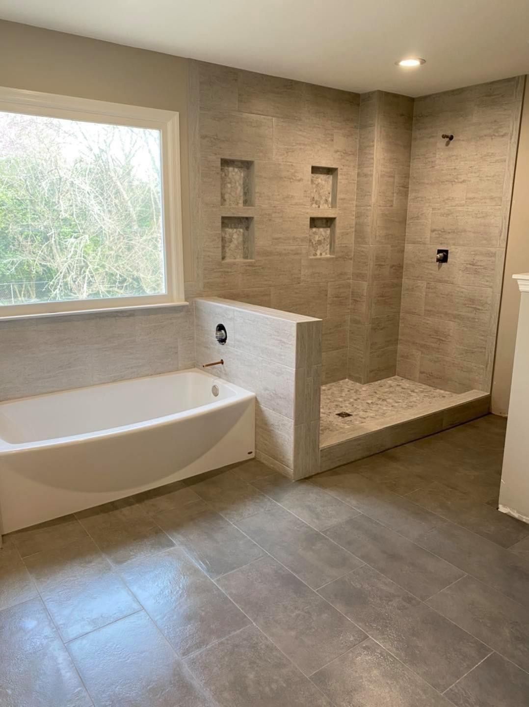 Bathroom with a white bathtub, tiled shower, and large window.
