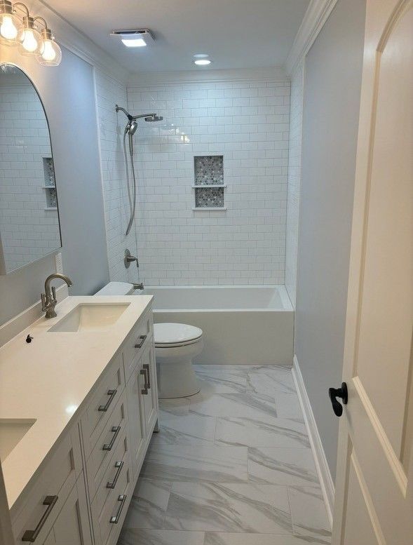 Bathroom with white vanity, toilet, and bathtub. Subway tile shower wall, gray and white marble floor.