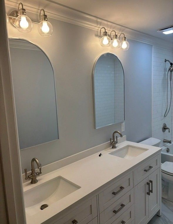 Bathroom with white double vanity, arched mirrors, and globe lights.