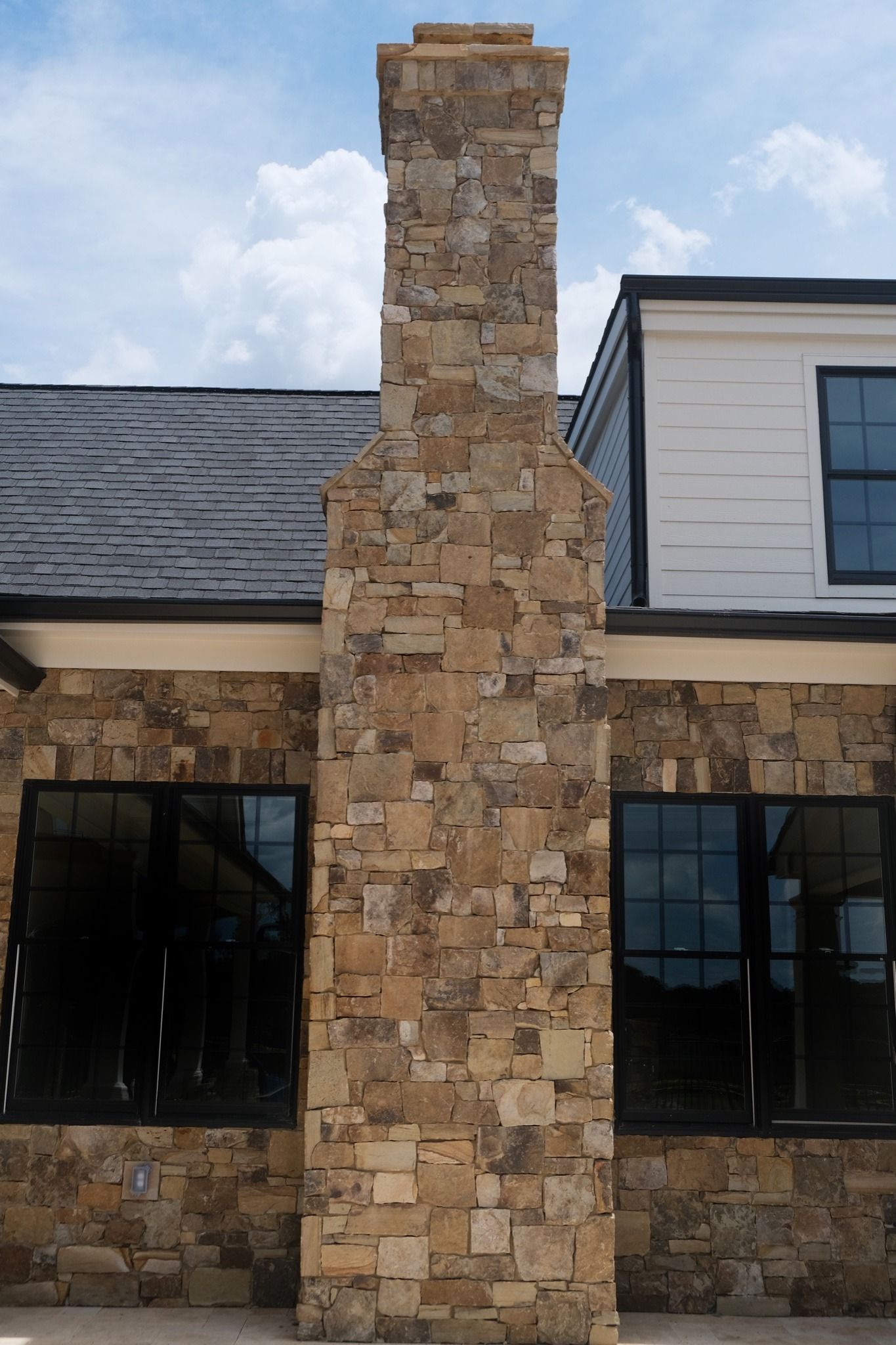 Stone chimney on a building with black windows and a black roof.
