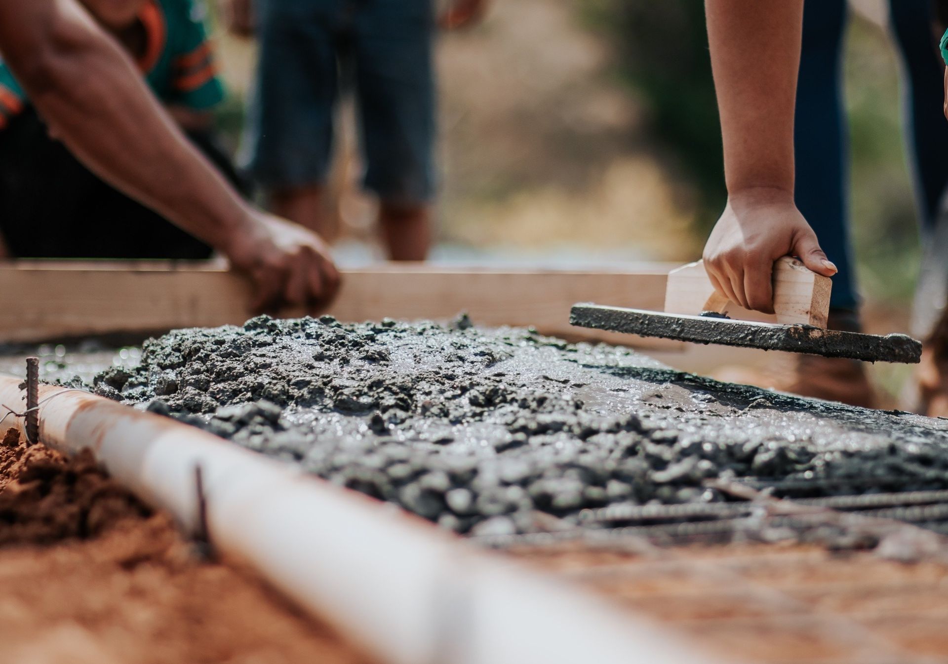 People smoothing wet concrete with a trowel, creating a pathway.