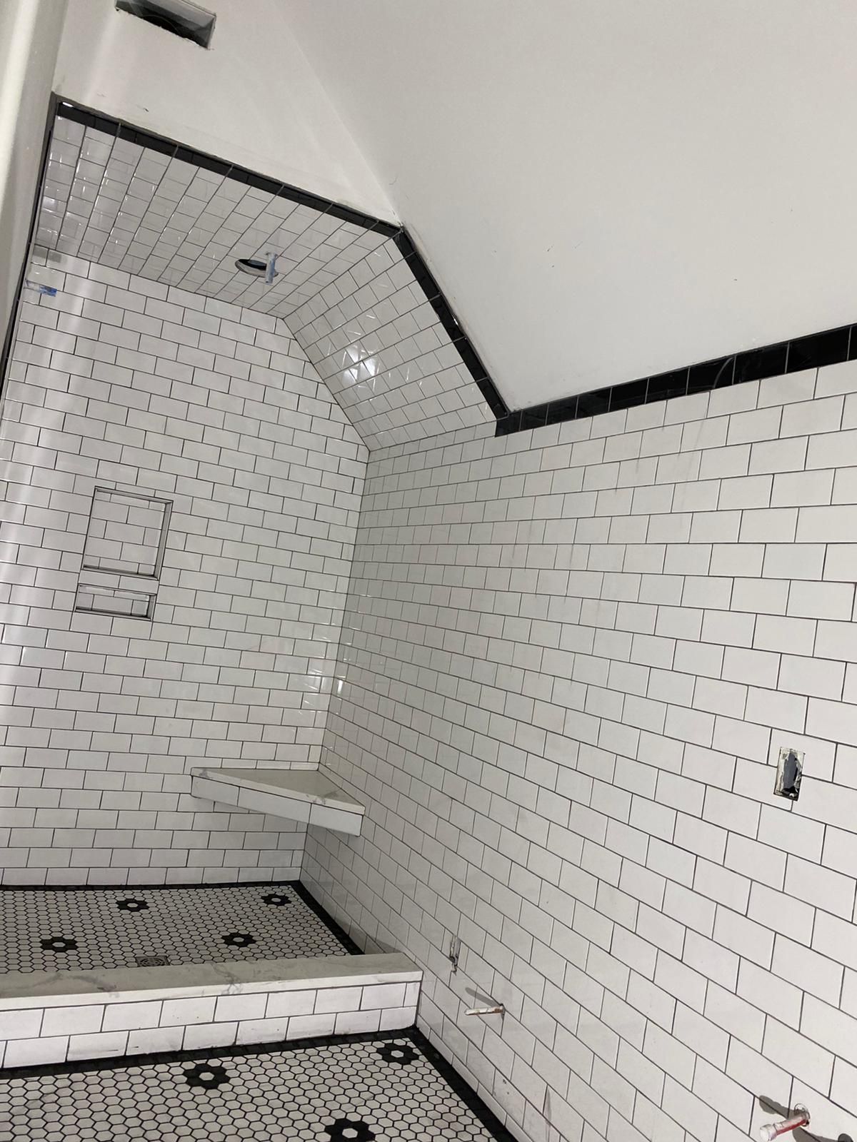 White subway-tiled shower with black trim. Black and white patterned floor. Recessed shelf and bench.