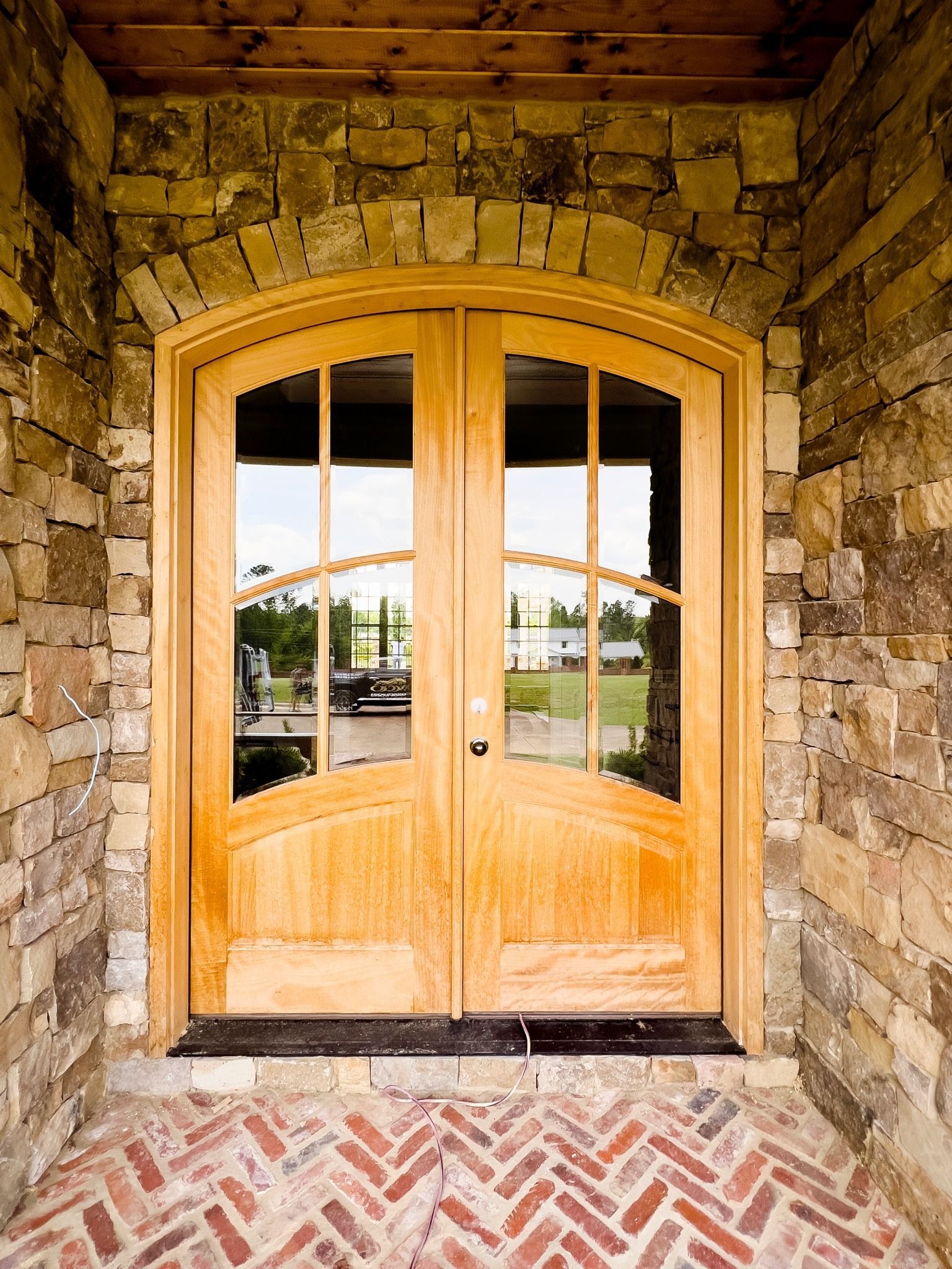 Wooden double doors with arched glass panels set in a stone archway, brick floor.