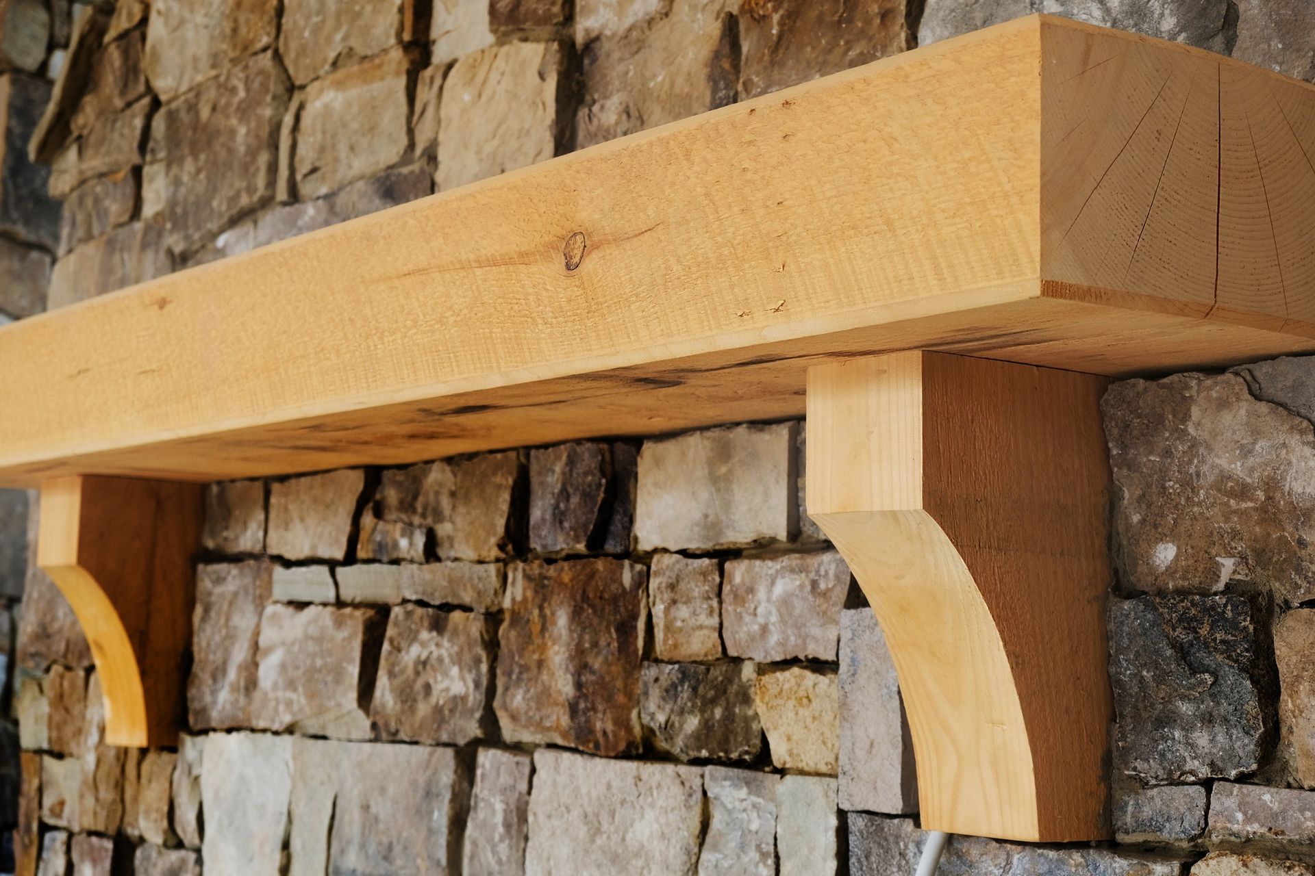 Wooden fireplace mantel supported by brackets, set against a stone wall.