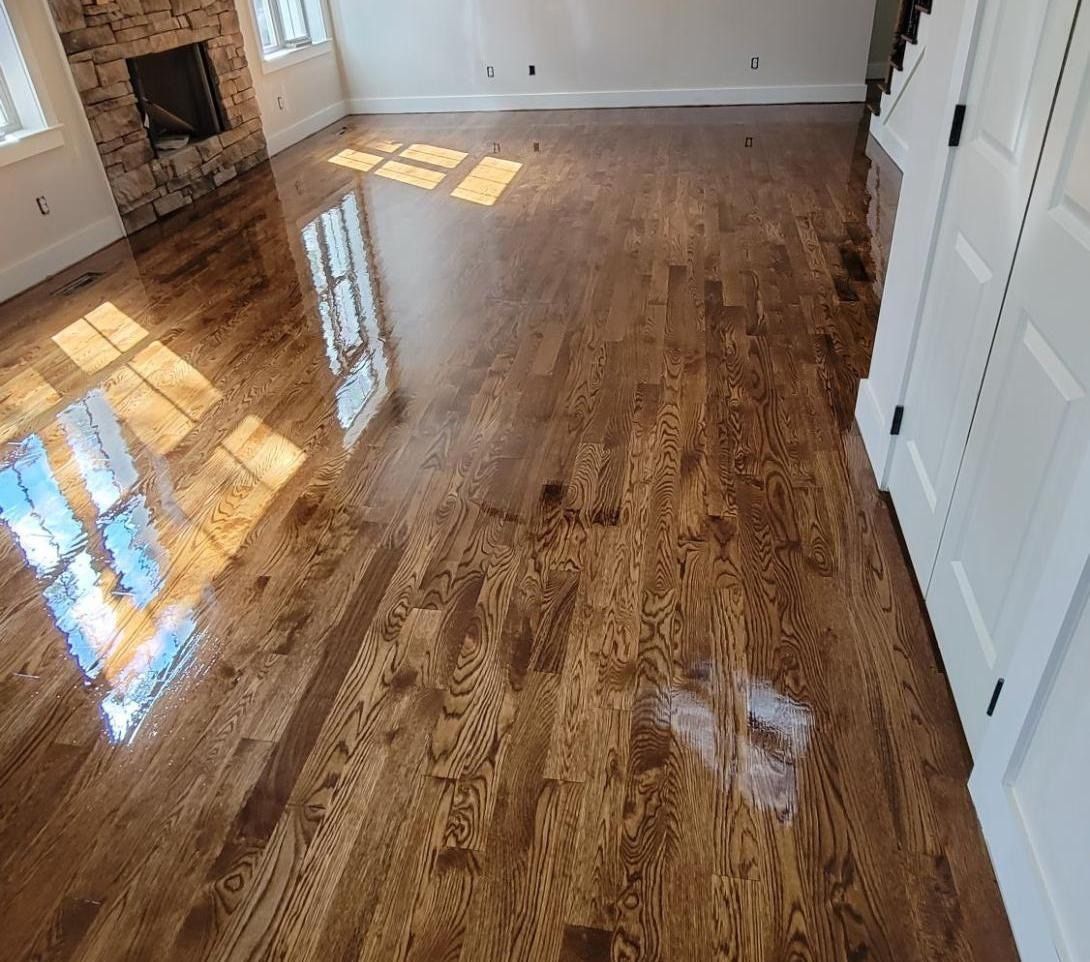 Glossy wooden floor reflecting sunlight in a room with a fireplace and white trim.