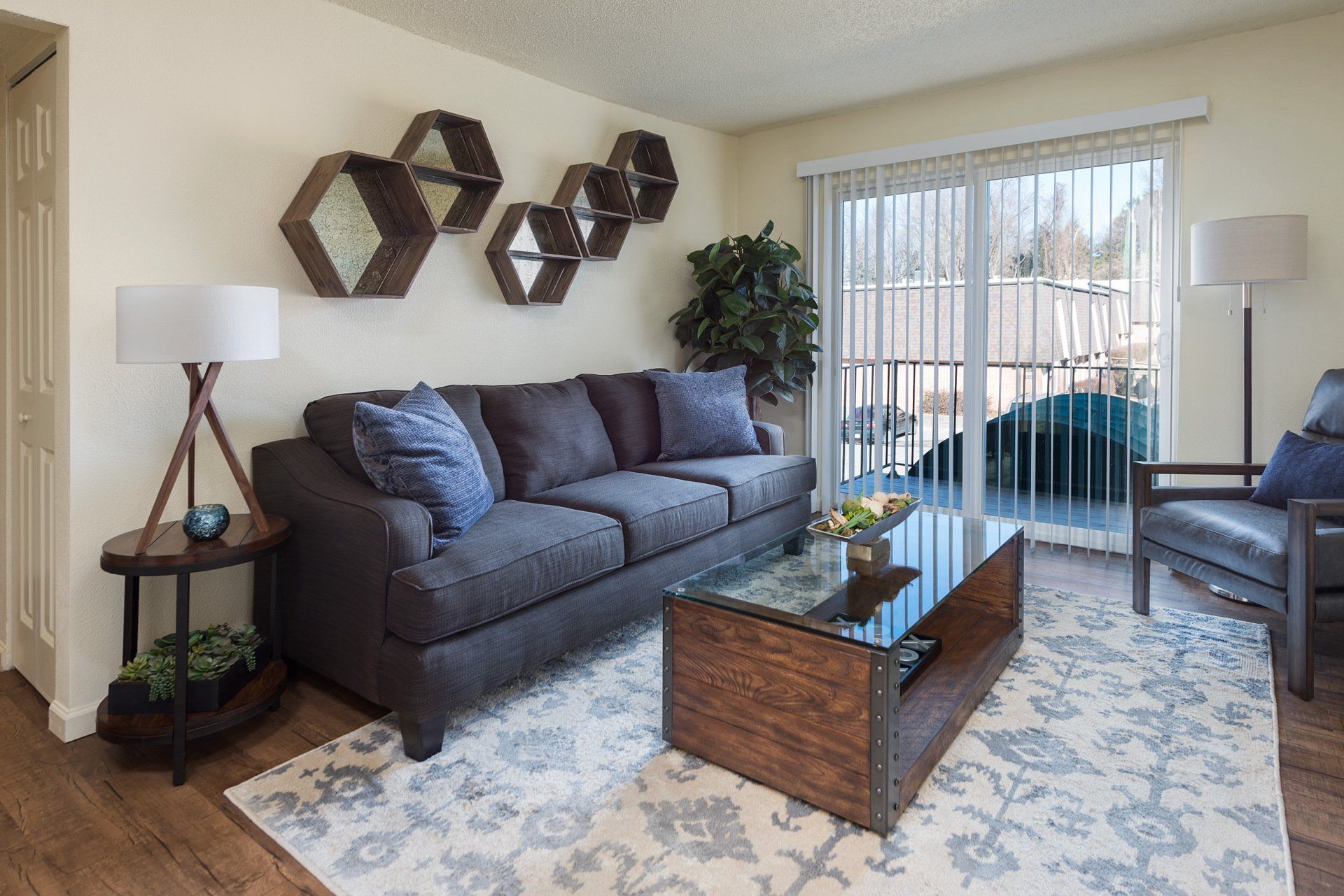 Living room with gray sofa, wood coffee table, patterned rug, lamps, wall decor, and sliding doors to a patio.