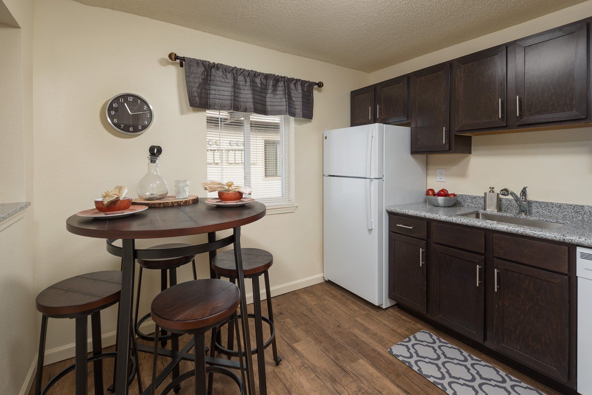 Compact kitchen with dark cabinets, a white fridge, and a small round table by the window