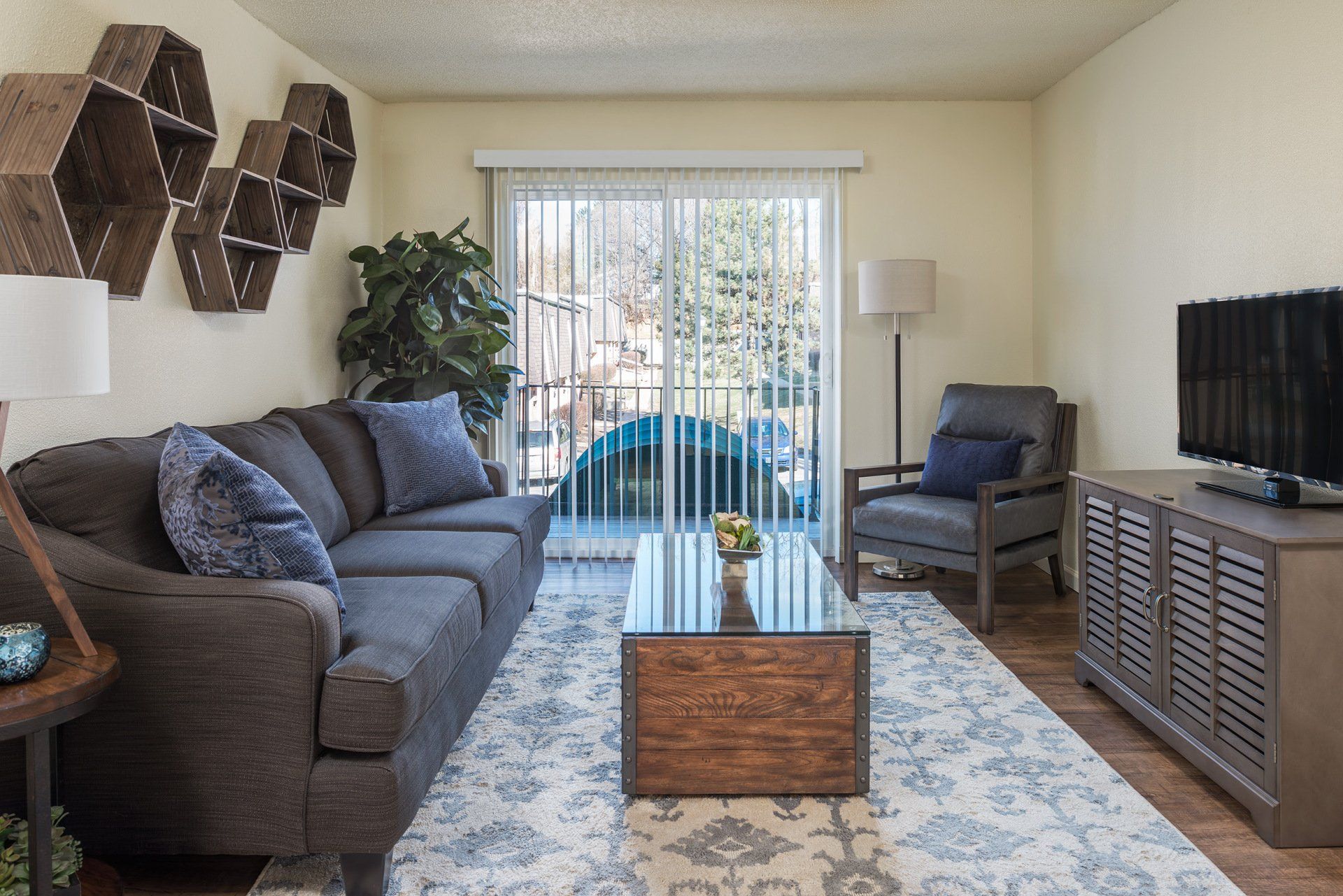 Modern living room with gray sofa, blue chair, TV, coffee table, and sliding glass doors to balcony