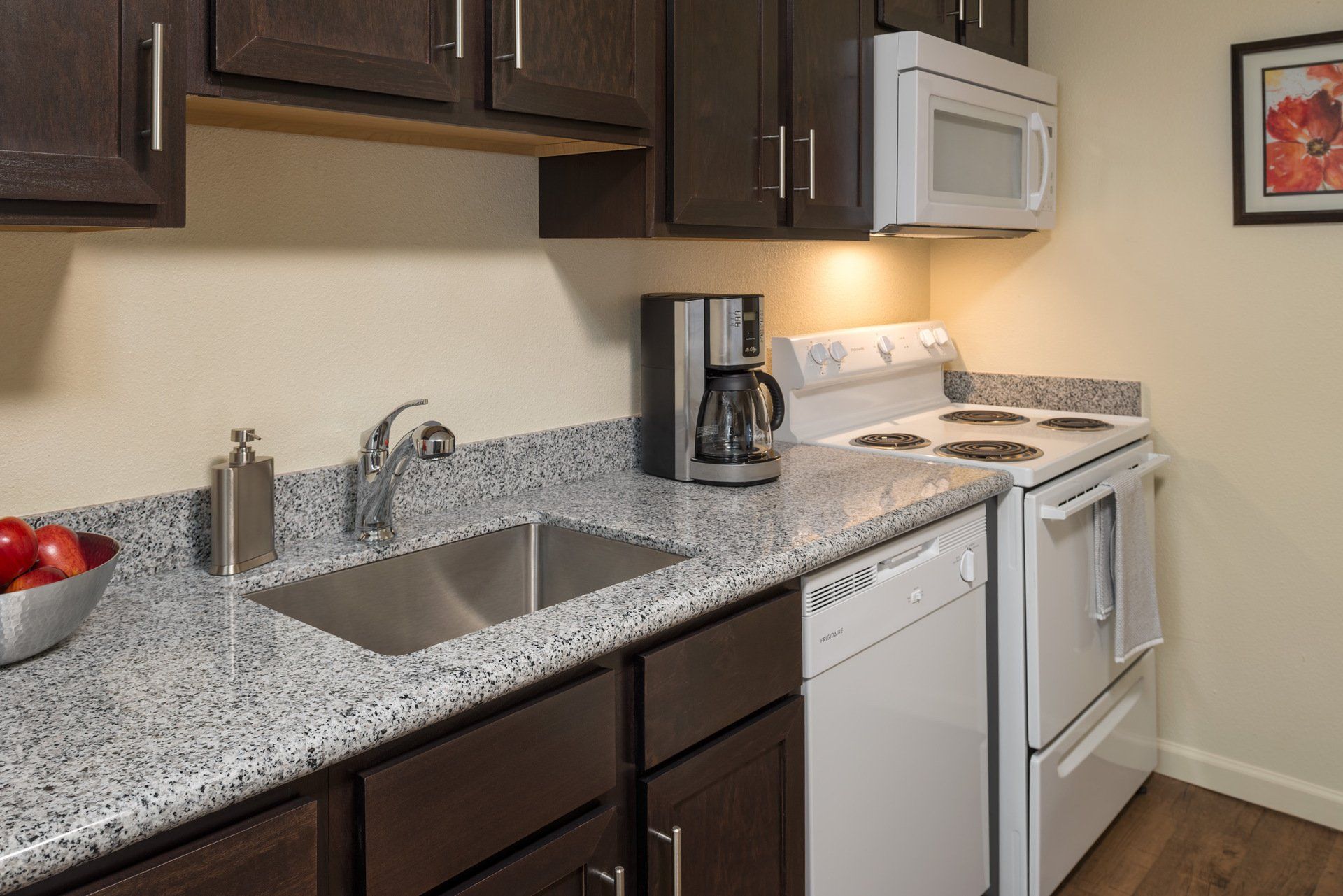 Small kitchen with speckled countertops, stainless sink, white stove, microwave, and coffee maker.