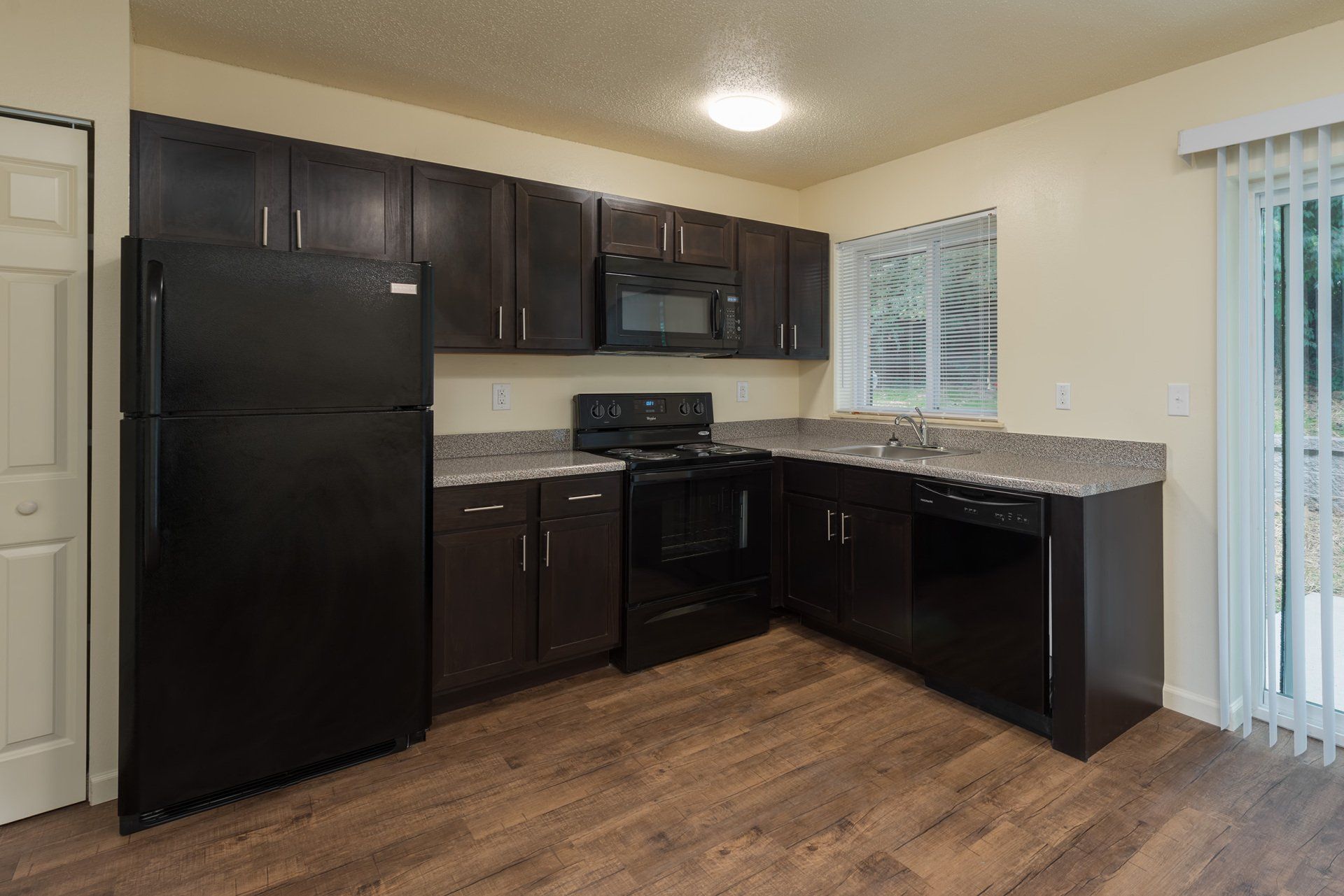 Small kitchen with black appliances, dark cabinets, granite counters, and wood flooring.